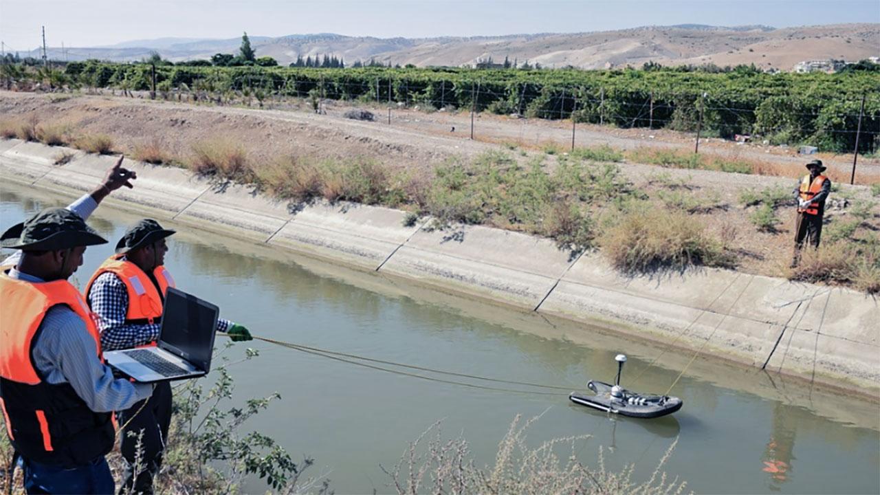 Two water flow engineers guide a measurement device down a narrow river in Jordan