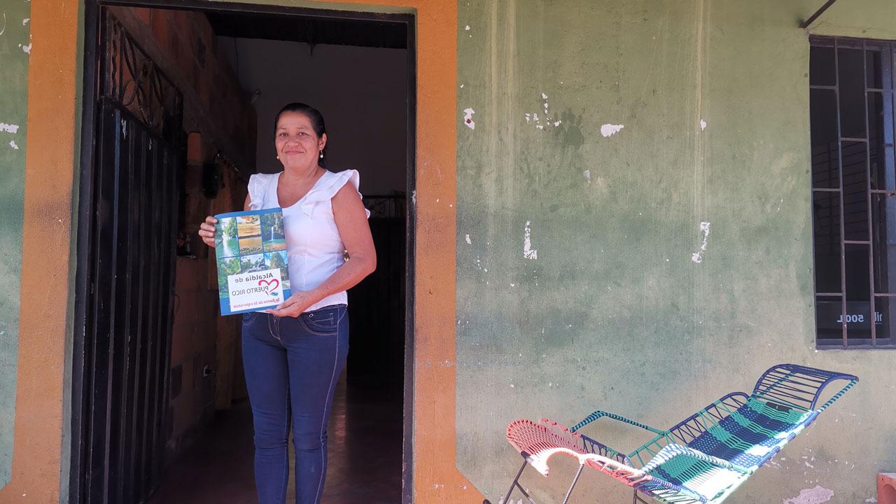 A woman stands in her doorway holding her land title