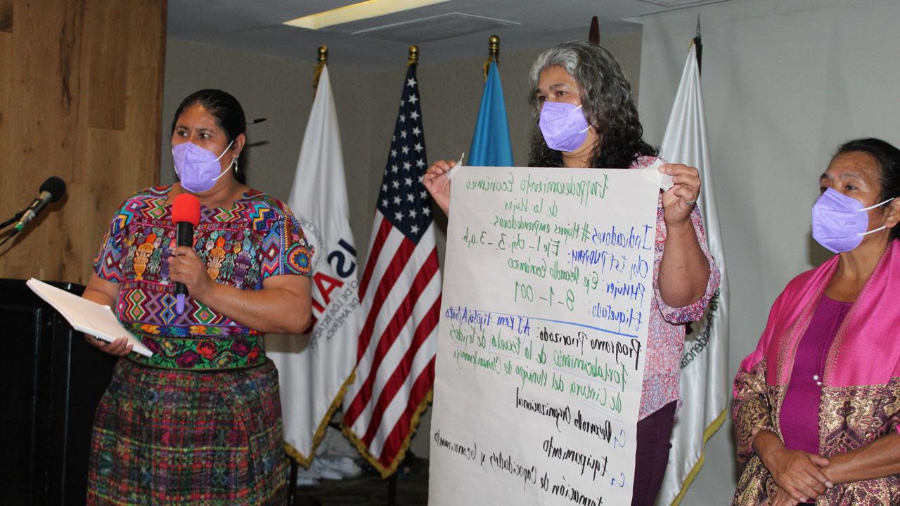 Three women hold a poster sharing their ideas for increasing female engagement in local decision-making spaces